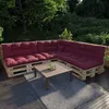 An outdoor seating area with a sectional sofa made of pallets and dark red cushions, a coffee table, and a rug. Produktbild-Vorschau