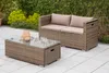 A patio set with a sofa and coffee table on a tiled patio, surrounded by greenery. Produktbild-Vorschau