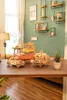 Wooden models of a tram, a car, and a carriage are displayed on a wooden table in a room with green walls and shelves. Produktbild-Vorschau