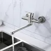 A stainless steel kitchen faucet mounted on a marble-tiled wall, with water flowing into a double sink. Podgląd zdjęcia produktu