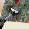 A vacuum cleaner is cleaning a colorful children's play mat with a street and house design. Produktbild-Vorschau
