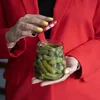 A person in a red jacket is opening a jar of pickles. Produktbild-Vorschau
