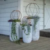 Three decorative planters with lights on a wooden deck in front of a white building. Produktbild-Vorschau