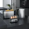 A breakfast set including a toaster, egg cooker, and kettle is displayed on a black countertop in a modern kitchen. Produktbild-Vorschau
