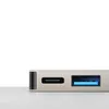 A close-up of a silver USB-C hub with a USB-C port and a blue USB 3.0 port, placed on a light gray surface against a white background. Produktbild-Vorschau