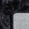 A close-up view of the corner of a black shaggy rug, showing the top fluffy side and the grey non-slip backing. Produktbild-Vorschau