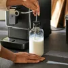 A person is using a coffee machine to froth milk in a glass bottle. Produktbild-Vorschau