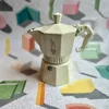 A cream-colored Bialetti Moka coffee maker is placed on a patterned surface with geometric shapes. Anteprima dell’immagine prodotto