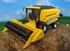 A toy model of a New Holland combine harvester sits on a dirt mound with a backdrop of a blue sky and green fields. Voir les images du produit