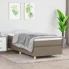 A taupe boxspring bed frame with a gray blanket and white pillow, placed on a light gray rug in a room with two framed plant pictures on the wall and a large potted plant. Podgląd zdjęcia produktu
