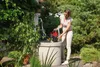 A woman is using a submersible pump next to a well in a garden. Podgląd zdjęcia produktu