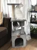 A white cat sits on a multi-level cat tree in a living room. Náhled obrázku produktu