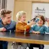 A father and two children are playing with a toy drone on a table. Produktbild-Vorschau