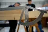 A close-up of a carpenter's angle measuring tool being used on a wooden beam, with two people blurred in the background. Produktbild-Vorschau