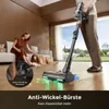 A woman is petting her dog while a cordless vacuum cleaner is being used to clean the floor. Produktbild-Vorschau