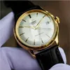 A close-up shot of a gold-colored Orient watch with a white face and a black leather strap, held by a gloved hand. Produktbild-Vorschau