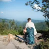 A person sitting on a bench in the mountains with a backpack and hiking poles. Anteprima dell’immagine prodotto
