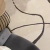 A close-up view of a rug with an abstract pattern, partially visible furniture, and a coffee table. Produktbild-Vorschau