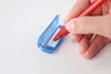 A hand holding a red pen and writing on a small piece of paper inside a blue plastic case. Produktbild-Vorschau