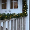 A garland with lights is draped over a wooden railing in front of a white door. Produktbild-Vorschau
