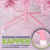 Close-up of the base of a pink artificial Christmas tree, showing the metal stand with protective caps on the feet. Text overlays highlight the feature of the caps. Produktbild-Vorschau