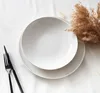 A white plate with black cutlery and dried grass on a white surface. Anteprima dell’immagine prodotto
