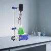 A laboratory setup with a magnetic stirrer mixing a green liquid in an Erlenmeyer flask, with other lab equipment in the background. Náhled obrázku produktu