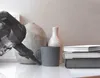 A cordless vacuum cleaner is shown on a shelf next to decorative items. Voir les images du produit