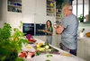 A couple in a modern kitchen, one person is taking a photo of the other who is holding a plate of food. Voir les images du produit