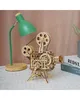 A wooden model film projector sits on a checkered surface next to a green desk lamp. Produktbild-Vorschau
