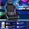 A gaming chair with LED lights and a remote control, set in a gaming room environment with a computer monitor and shelves. Produktbild-Vorschau