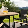 An outdoor dining set with a round table and chairs on a wooden deck, with a scenic view of hills and trees in the background. Produktbild-Vorschau