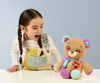 A young girl with braided hair looks excitedly at a stuffed teddy bear. Podgląd zdjęcia produktu