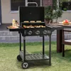 A gas grill is set up on a grassy lawn in front of a house, with food on the grill and a table with food in the background. Produktbild-Vorschau