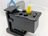 A close-up view of a black printer ink cartridge with a yellow nozzle and a clear tube attached. Produktbild-Vorschau
