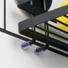 A close-up view of a black metal shower shelf with suction cups attached to a tiled wall. A yellow sponge is visible on the shelf. Podgląd zdjęcia produktu