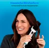 A woman is smiling while using a hair straightening brush on her hair against a blue background. Produktbild-Vorschau