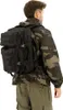 A person wearing a camouflage jacket and olive green pants, carrying a black backpack. Náhled obrázku produktu