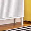 A close-up view of the bottom section of a white fluted cabinet, showing its legs and the floor beneath. A yellow cabinet is visible to the right, and a striped rug is in the foreground. Náhľad obrázku produktu