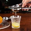 A hand is using a manual citrus juicer to squeeze juice into a glass with lemon slices. Produktbild-Vorschau