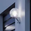 A white outdoor wall light with a clear globe is mounted on a light gray wall. Anteprima dell’immagine prodotto