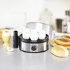 An egg cooker with several eggs, a soft-boiled egg in an egg cup, and a bread roll with jam on a countertop. Produktbild-Vorschau
