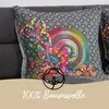 A close-up of a decorative pillow with a colorful mandala and floral pattern, placed on a sofa. A beige band at the bottom contains a cotton logo and text. Produktbild-Vorschau