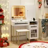 A white vanity table with a lighted mirror, stool, and drawers, decorated for Christmas with stockings, garland, and gifts. Voir les images du produit