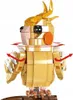 A gold-colored toy cockatiel bird made of building blocks, standing on a brown perch. Red arrows indicate movement of the wings and head. Náhľad obrázku produktu