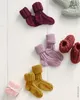 A collection of knitted baby socks in various colors arranged on a white wooden surface. Produktbild-Vorschau