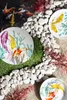 A close-up overhead view of decorative plates with koi fish designs, arranged on a surface with white stones, artificial grass, and red decorative plants. Podgląd zdjęcia produktu