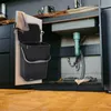 A black hanging trash can with a lid is attached to the inside of a cabinet door under a kitchen sink. Voir les images du produit