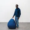 A young man stands next to a large blue beanbag chair. Voir les images du produit
