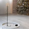 A spiral Christmas tree with gold LED lights and a star on top, placed on a white table next to a larger, decorated Christmas tree. Voir les images du produit